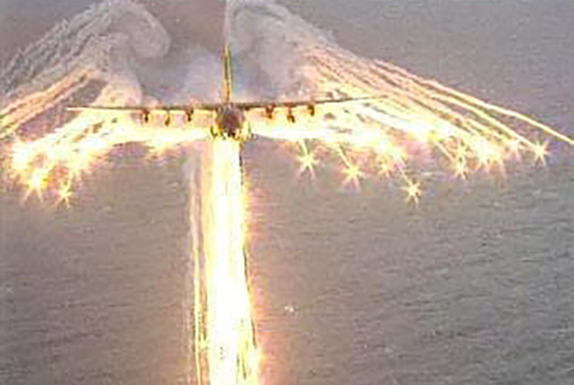 C-130 Hercules releasing a symmetric volley of defensive flares over water